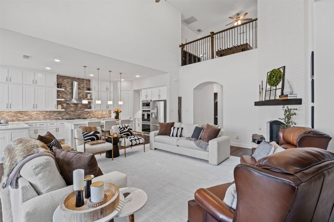Living room with arched walkways, a fireplace, light wood finished floors, a ceiling fan, and baseboards | Image 9