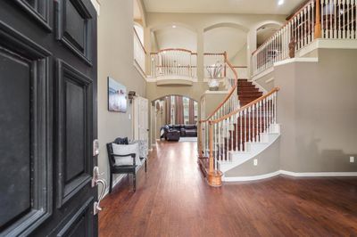 This is a spacious entryway with high ceilings, featuring hardwood floors and an elegant staircase leading to a second-floor landing. The neutral color palette provides a warm, inviting atmosphere. | Image 3