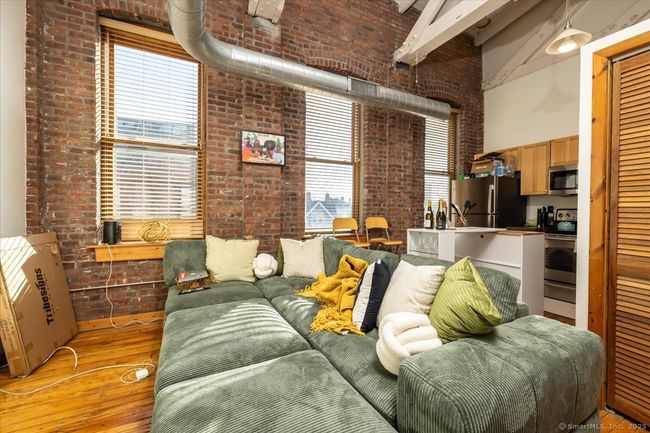 A stylish loft-style interior with exposed brick walls, high ceilings with industrial ductwork, polished hardwood floors, rustic wood doors, and a cozy open layout featuring large windows that bring in natural light | Image 6