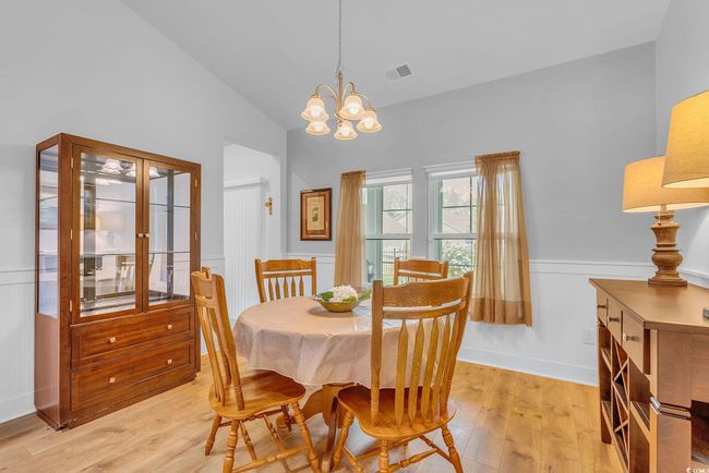 Dining room with visible vents, an inviting chandelier, light wood-type flooring, vaulted ceiling, and a wainscoted wall | Image 16