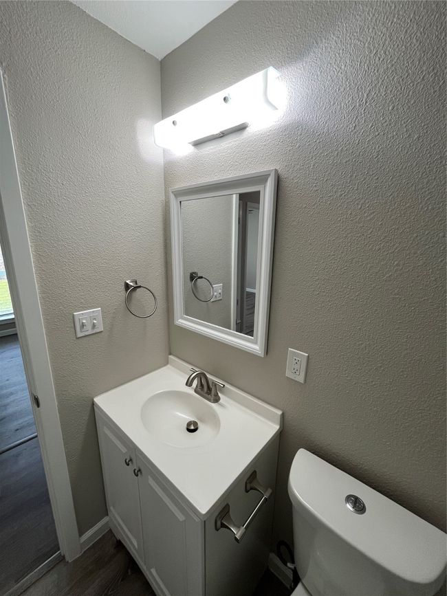 Half bathroom with vanity, toilet, a textured wall, and wood finished floors | Image 10