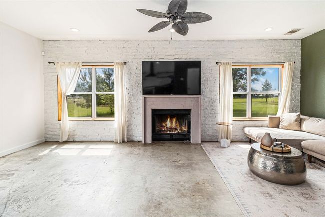 Living room with visible vents, a ceiling fan, concrete floors, and a lit fireplace | Image 11