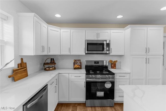 Kitchen featuring appliances with stainless steel finishes, white cabinets, backsplash, light wood-style floors, and light stone countertops | Image 11
