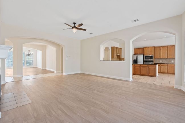 Unfurnished living room with light wood finished floors, ceiling fan with notable chandelier, visible vents, and baseboards | Image 17