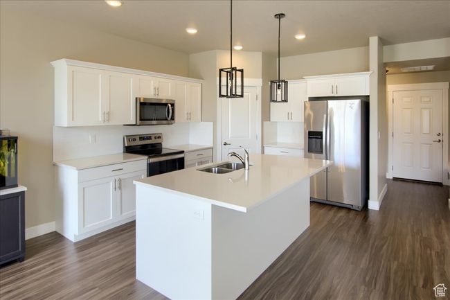 Kitchen with a sink, appliances with stainless steel finishes, a kitchen island with sink, dark wood finished floors, and white cabinetry | Image 9