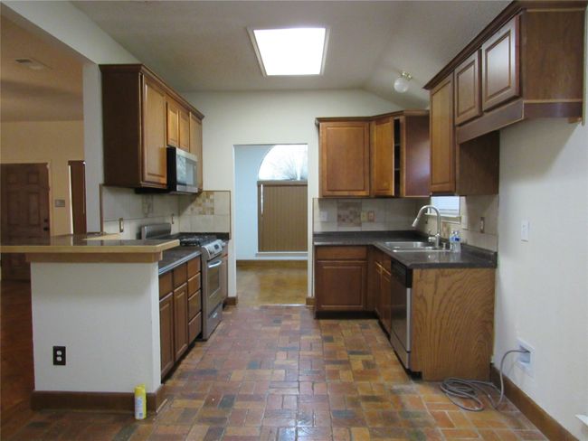 Kitchen featuring stainless steel appliances, a sink, dark countertops, baseboards, and decorative backsplash | Image 7