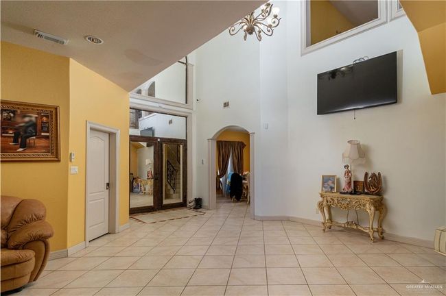 Living room featuring a textured ceiling, a towering ceiling, light tile patterned floors, and a chandelier | Image 11