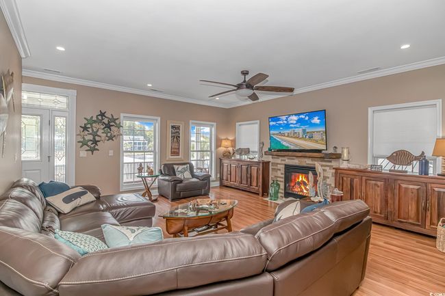 Living area with light wood finished floors, a ceiling fan, crown molding, a fireplace, and recessed lighting | Image 12