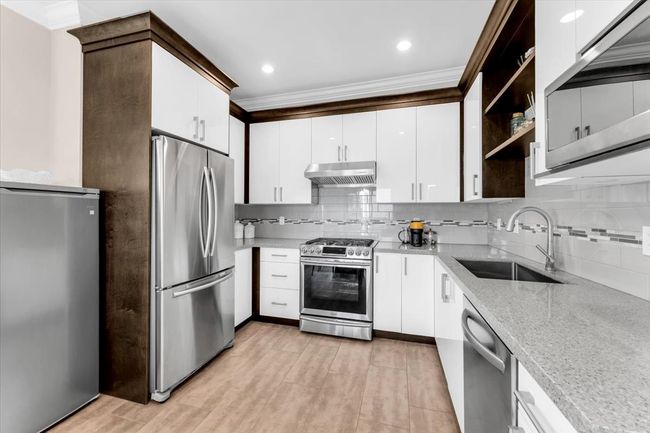 Kitchen with stainless steel appliances, under cabinet range hood, ornamental molding, backsplash, and light wood-style flooring | Image 8