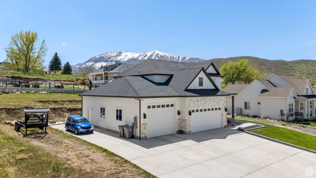 View of side of home with concrete driveway, an attached garage, stone siding, roof with shingles, and a mountain view | Image 4