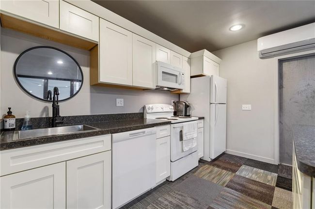 Kitchen with a wall mounted AC, white appliances, sink, and white cabinetry | Image 18