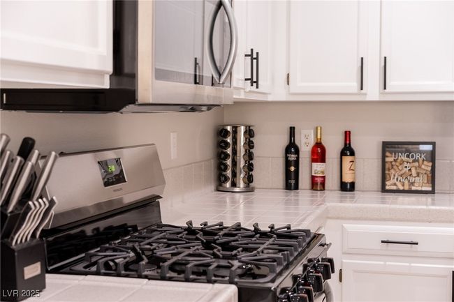 Room details featuring tile countertops, white cabinets, stainless steel appliances, and tasteful backsplash | Image 16