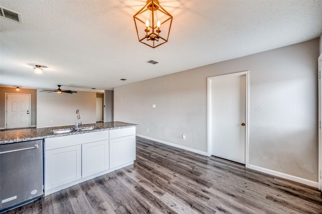Kitchen featuring a sink, dishwasher, wood finished floors, white cabinetry, and a textured ceiling | Image 8