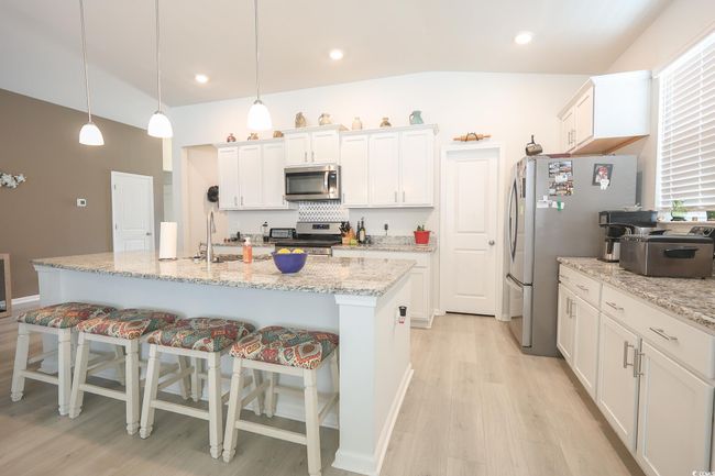 Kitchen featuring a breakfast bar, light wood finished floors, white cabinetry, and appliances with stainless steel finishes | Image 5
