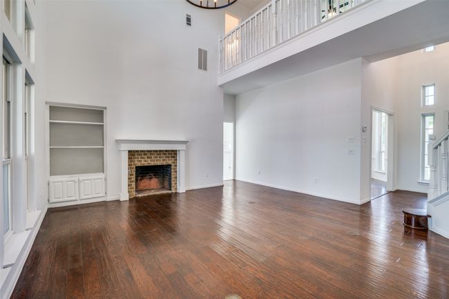 Unfurnished living room featuring a towering ceiling, a fireplace, hardwood / wood-style floors, baseboards, and a chandelier | Image 8