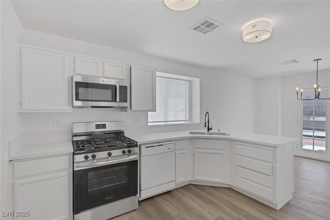 Kitchen with stainless steel appliances, a peninsula, a chandelier, light wood-type flooring, and light countertops | Image 13