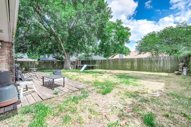 Spacious backyard with a wooden deck, mature trees providing shade, and a privacy fence. Ideal for outdoor activities and relaxation. | Image 23