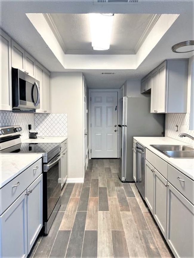 Kitchen with appliances with stainless steel finishes, a raised ceiling, a sink, ornamental molding, and light countertops | Image 6