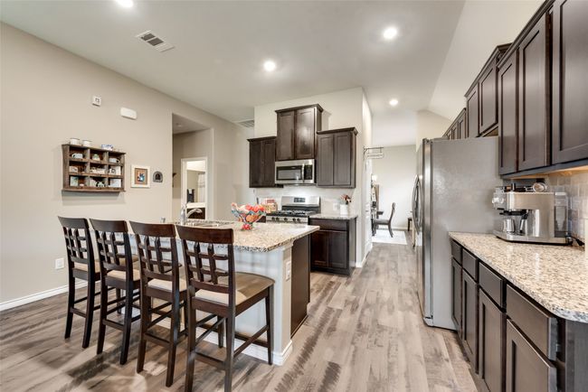 Kitchen featuring appliances with stainless steel finishes, light wood-style floors, dark brown cabinetry, an island with sink, and a kitchen breakfast bar | Image 14