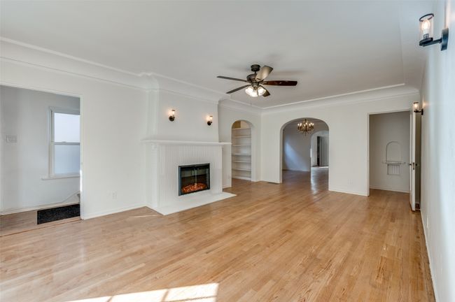 Unfurnished living room featuring built in shelves, a fireplace with flush hearth, a ceiling fan, light wood-style flooring, and arched walkways | Image 6