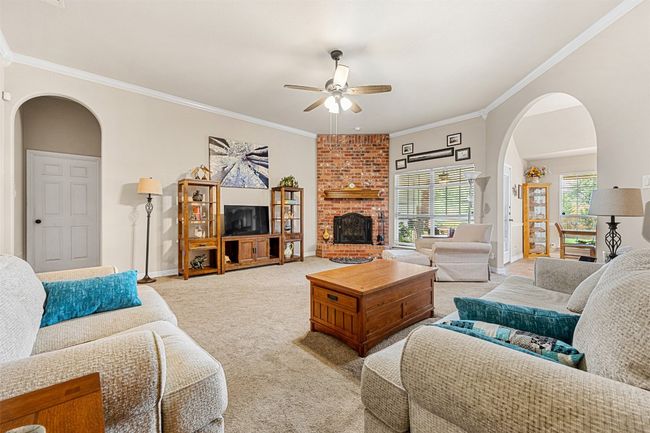 Living room with ceiling fan, arched walkways, light carpet, crown molding, and baseboards | Image 7