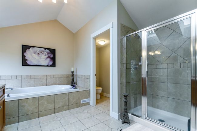 Full bath featuring toilet, tile patterned floors, vaulted ceiling, a bath, and a stall shower | Image 20