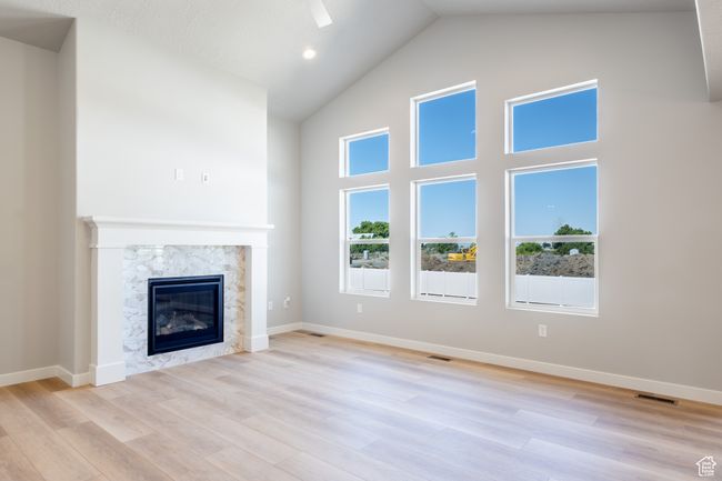 Unfurnished living room featuring high vaulted ceiling, a high end fireplace, and light wood-style floors | Image 13