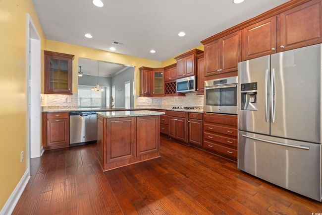 Kitchen with dark wood finished floors, light stone countertops, glass insert cabinets, decorative backsplash, and stainless steel appliances | Image 7