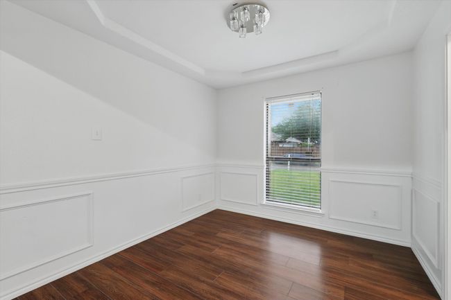 Empty room featuring a tray ceiling, dark wood-style floors, and wainscoting | Image 4