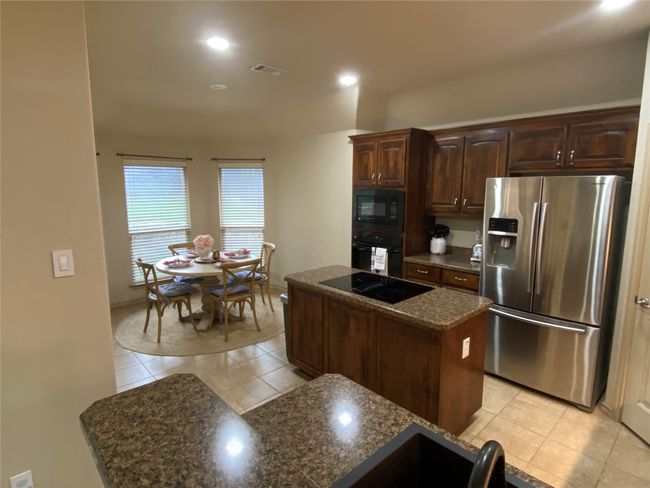Kitchen featuring light tile patterned flooring, a center island, dark brown cabinetry, and black appliances | Image 12