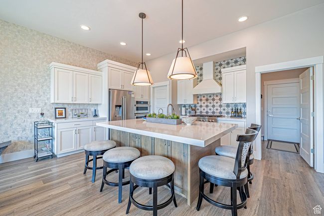 Kitchen with custom exhaust hood, appliances with stainless steel finishes, a breakfast bar area, white cabinets, and wallpapered walls | Image 13