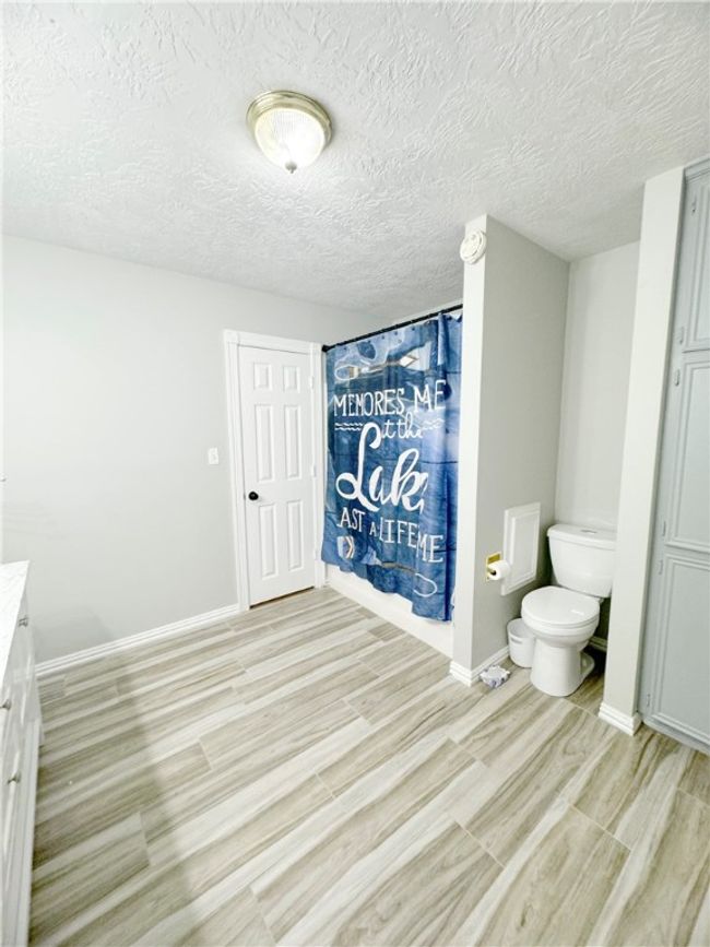 Bathroom with wood finished floors, a textured ceiling, vanity, a shower with curtain, and toilet | Image 9