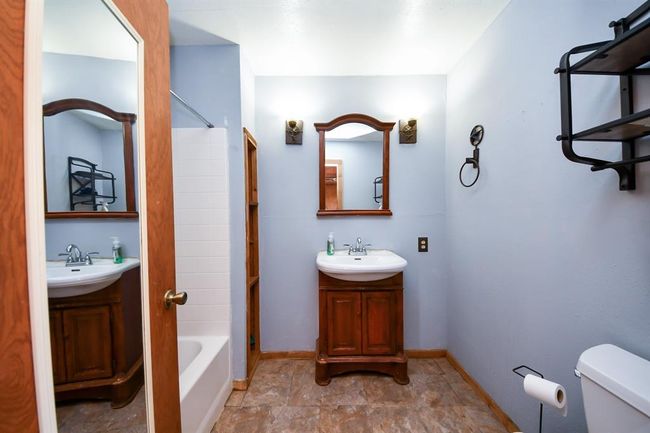 The apartment's bath is bathed in cool tones and features a built-in wooden shelf to the left of the sink. | Image 23