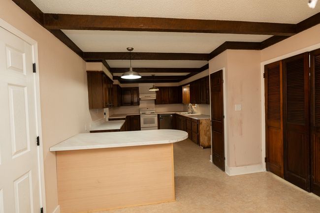 Kitchen featuring white electric stove, beam ceiling, light countertops, a peninsula, and light floors | Image 12