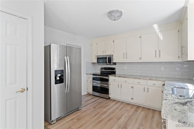 Kitchen with stainless steel appliances, backsplash, light wood-style flooring, white cabinetry, and light stone countertops | Image 7