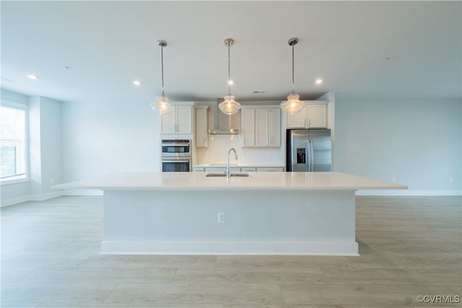 Kitchen with stainless steel appliances, wall chimney exhaust hood, a sink, a center island with sink, and baseboards | Image 8