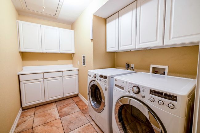 Laundry Room with washer and clothes dryer, attic access, light tile floors, baseboards, and cabinet storage | Image 38