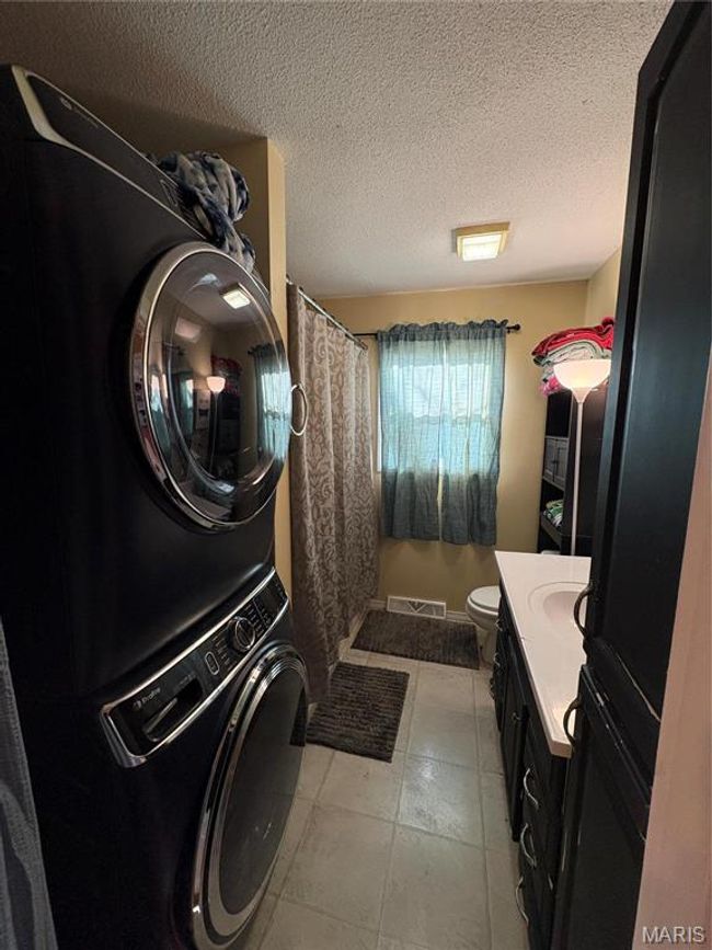 Washroom with light tile patterned floors, visible vents, a sink, a textured ceiling, and stacked washing maching and dryer | Image 16