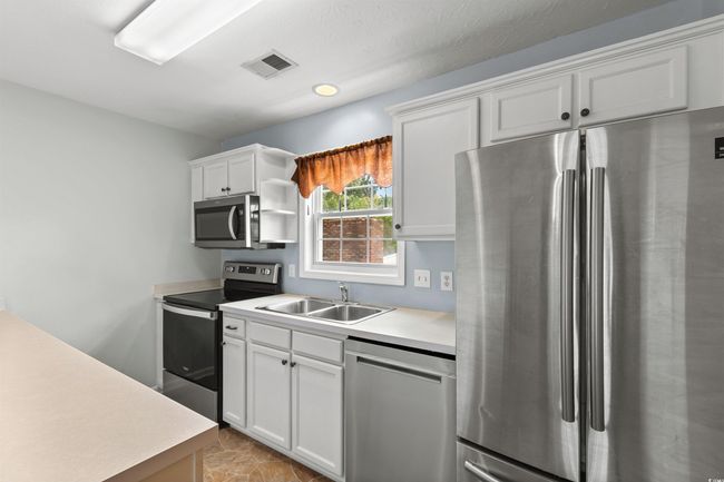Kitchen with stainless steel appliances, light countertops, white cabinets, and open shelves | Image 8
