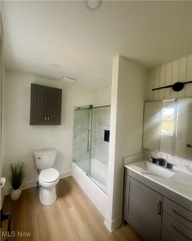 Full bathroom featuring vanity, baseboards, toilet, bath / shower combo with glass door, and wood finished floors | Image 11