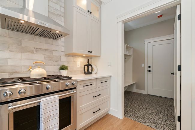 Kitchen featuring stainless steel range with gas cooktop, wall chimney range hood, light countertops, and decorative backsplash | Image 7