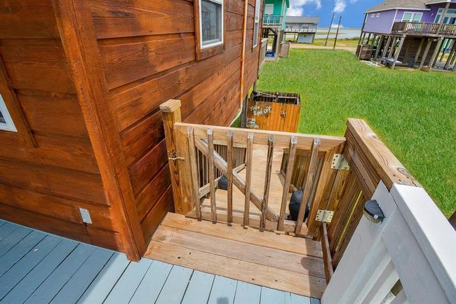 The stairs lead down to a grassy area, with views of nearby homes and a bay view in the background. The deck features a safety gate, adding a rustic charm to the outdoor space. | Image 20