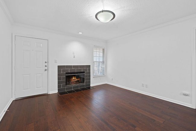 Unfurnished living room featuring dark wood-type flooring, a textured ceiling, a fireplace, crown molding, and baseboards | Image 9