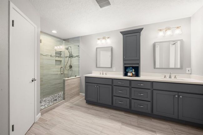 Luxurious walk-in shower features seamless glass, a soothing pebble floor, built-in seat, a convenient shampoo nook, and floor-to-ceiling tile for a spa-like experience. | Image 26