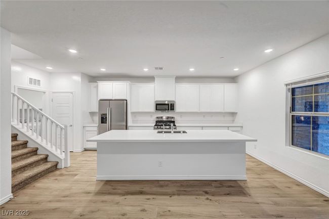 Kitchen with light wood finished floors, stainless steel appliances, light countertops, white cabinets, and an island with sink | Image 12