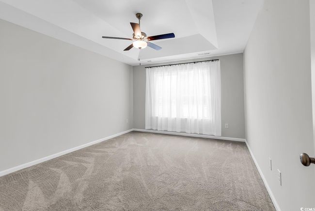 Carpeted empty room featuring ceiling fan, baseboards, and a tray ceiling | Image 26