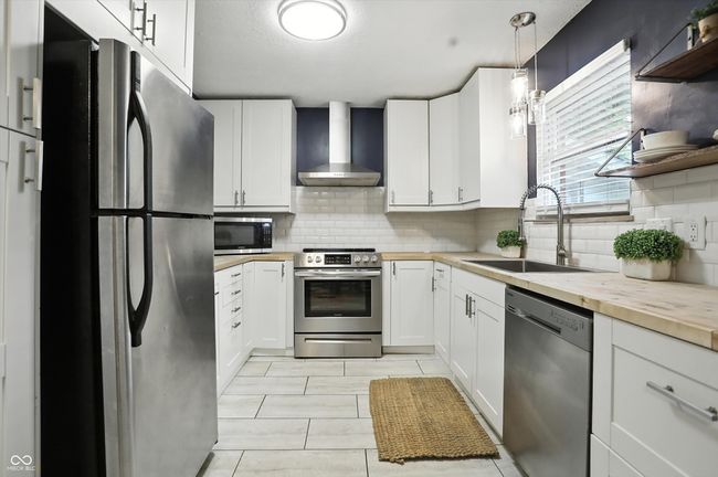 kitchen with stainless steel appliances, wall chimney exhaust hood, wooden counters, and backsplash | Image 7