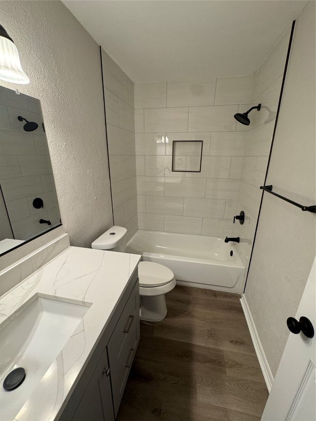 Full bathroom with a textured wall, wood finished floors, vanity, toilet, and shower / bath combination | Image 13