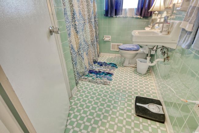 Full bathroom with toilet, curtained shower, tile walls, tile patterned floors, and a sink | Image 21
