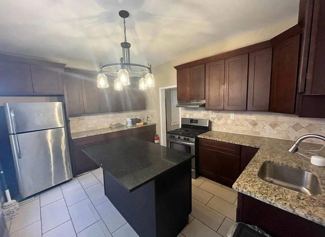 Kitchen with a chandelier, stainless steel appliances, under cabinet range hood, backsplash, and a sink | Image 6